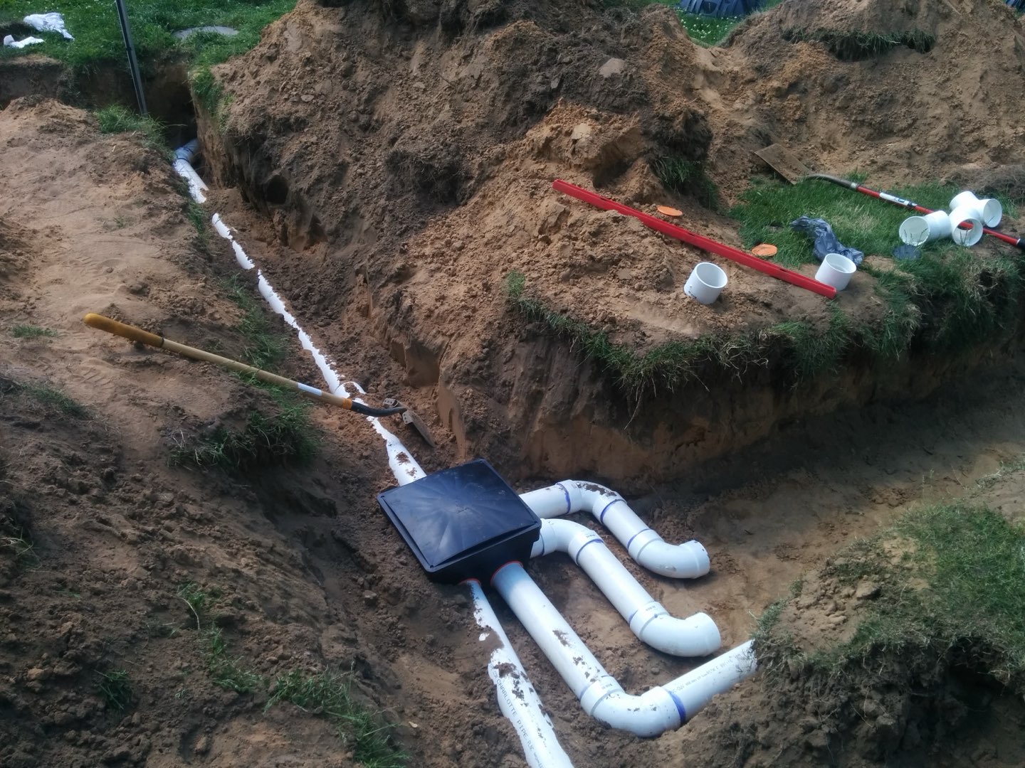 White PVC pipes branching from a black distribution box in an open trench.